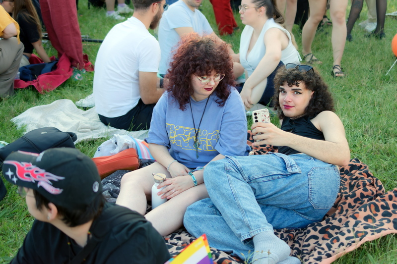 18 - People attendees at a public Pride, gathered on a grassy field, with a focus on individuals relaxing on a blanket